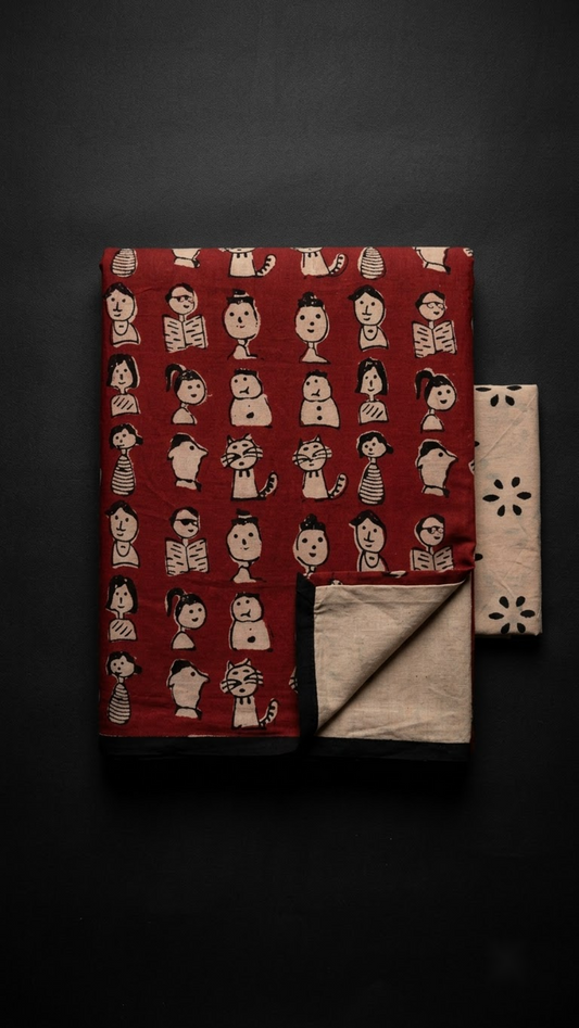 Red character print cotton saree with black border and ivory floral blouse, folded on charcoal background