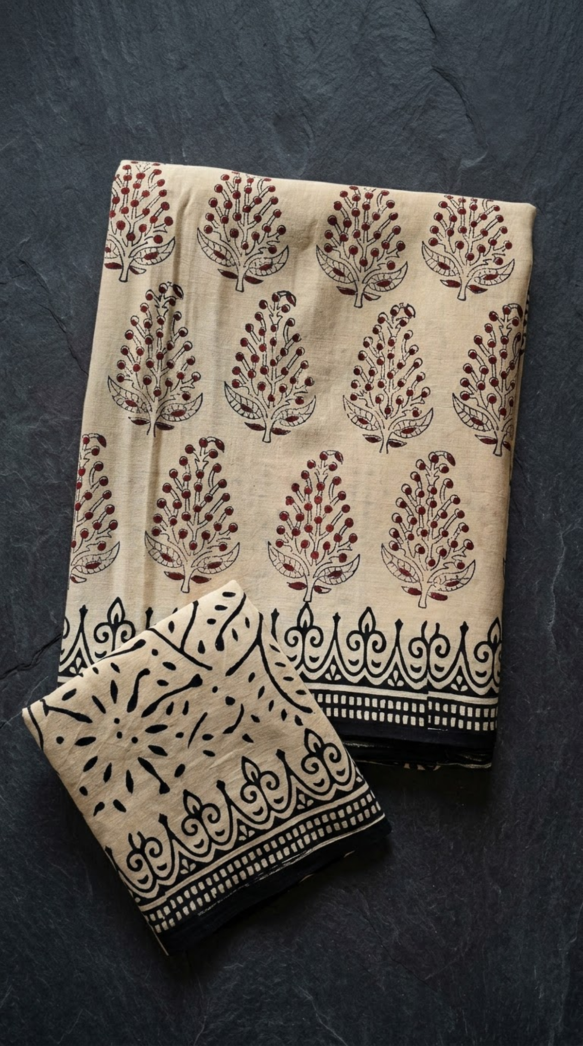 Ivory cotton saree with muted red and black botanical sprigs and a black border, folded on charcoal