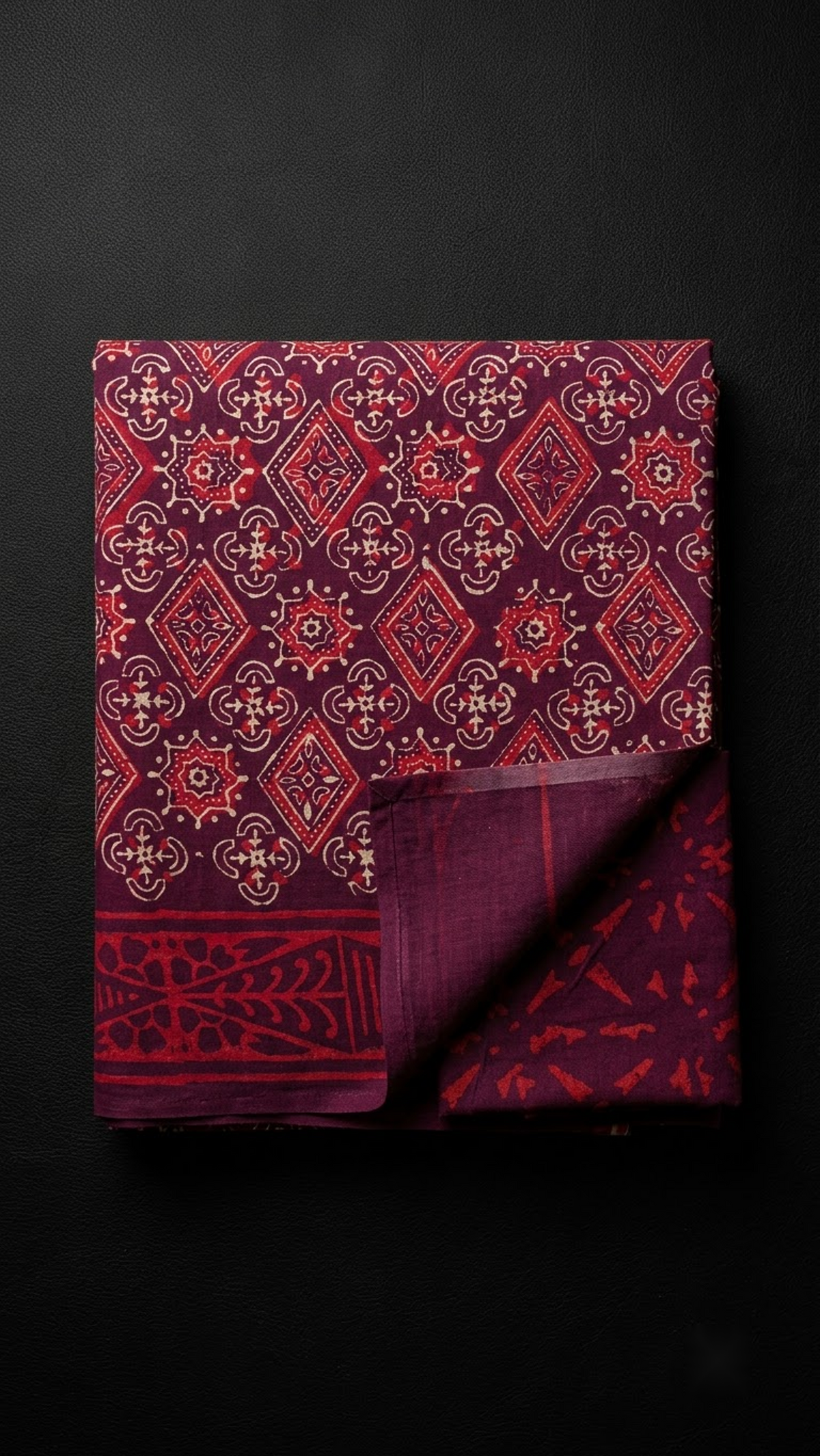 Burgundy cotton saree with a floral geometric print, red patterned border, and burgundy abstract-print blouse piece, folded on a charcoal background
