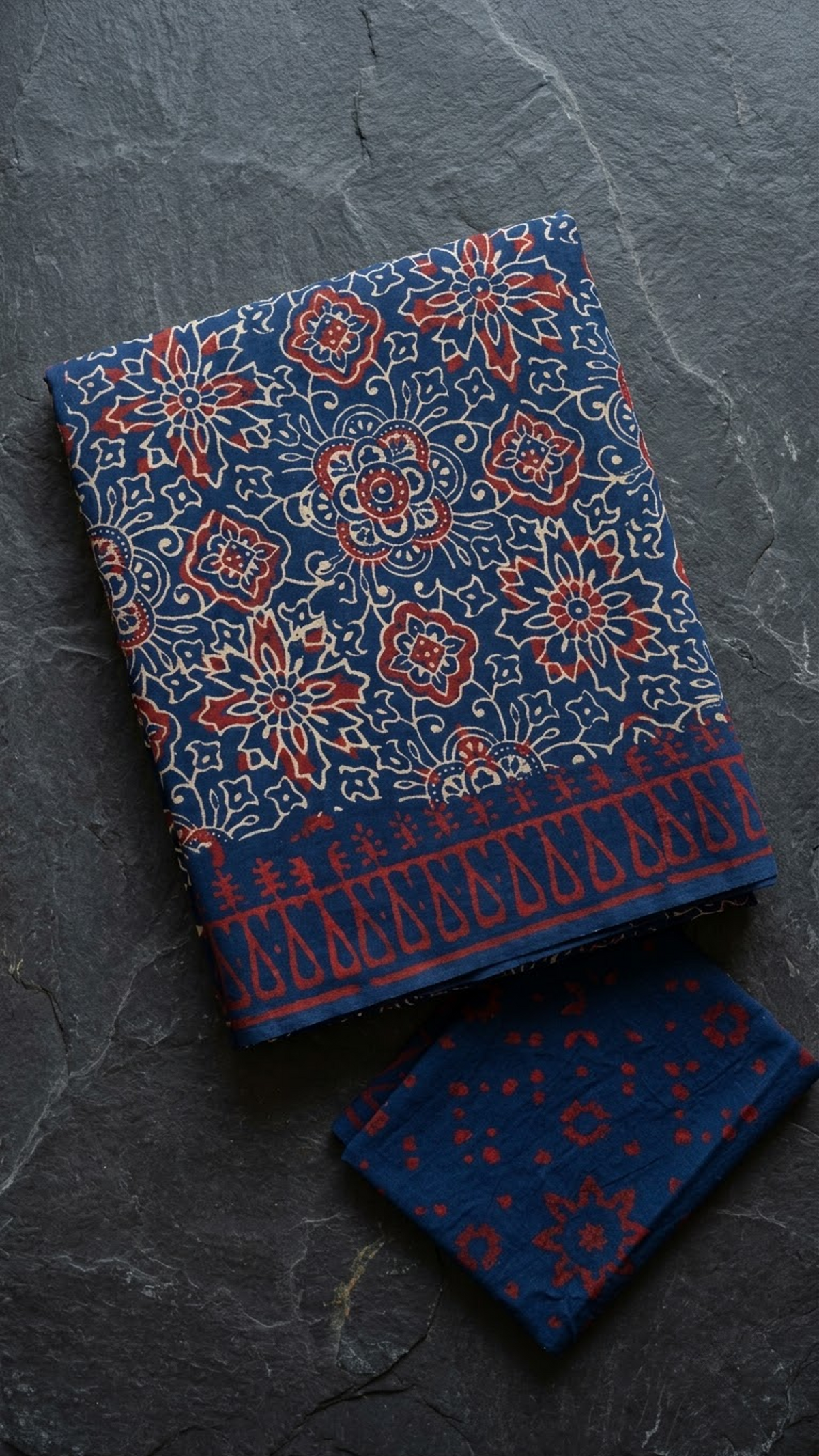 Navy cotton saree with red and ivory floral medallions and red border, folded on charcoal