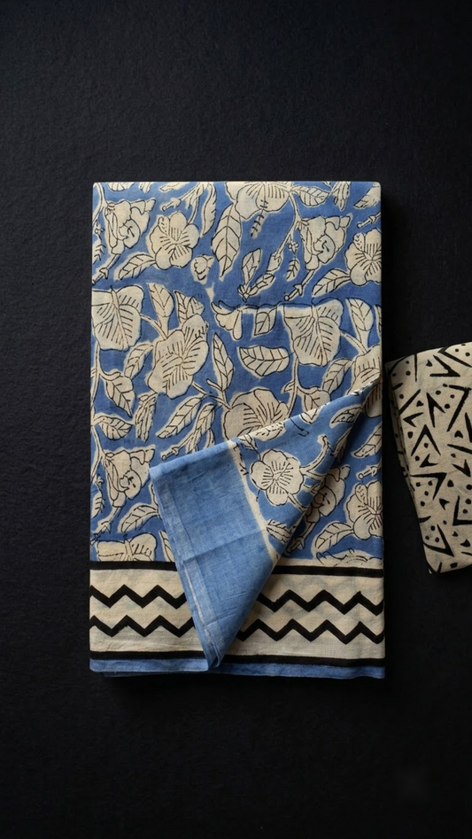 Blue cotton saree with ivory botanical print, black chevron border, and ivory geometric blouse piece, folded on a charcoal background