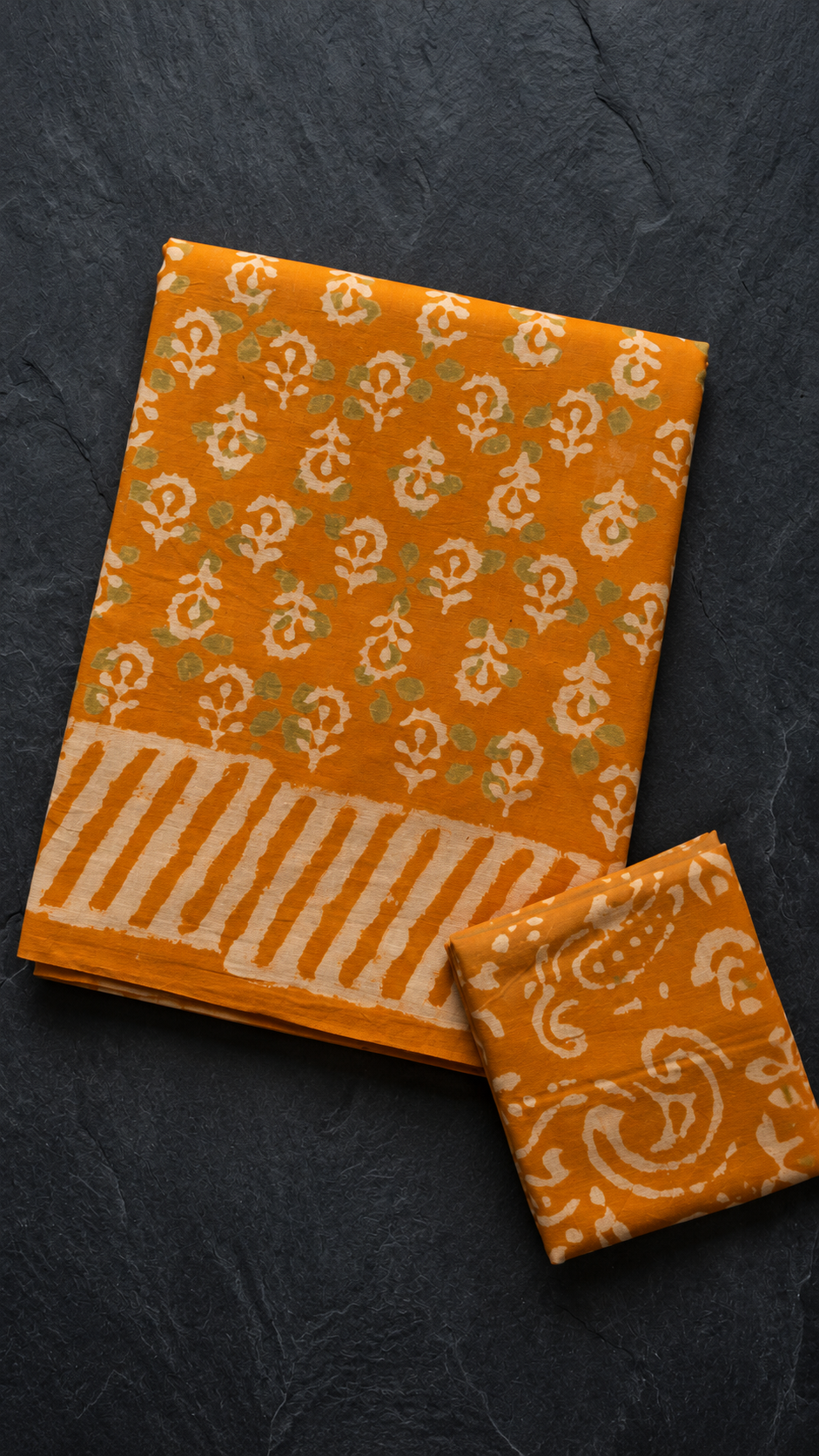 Orange cotton saree with ivory paisleys and striped border, folded on charcoal