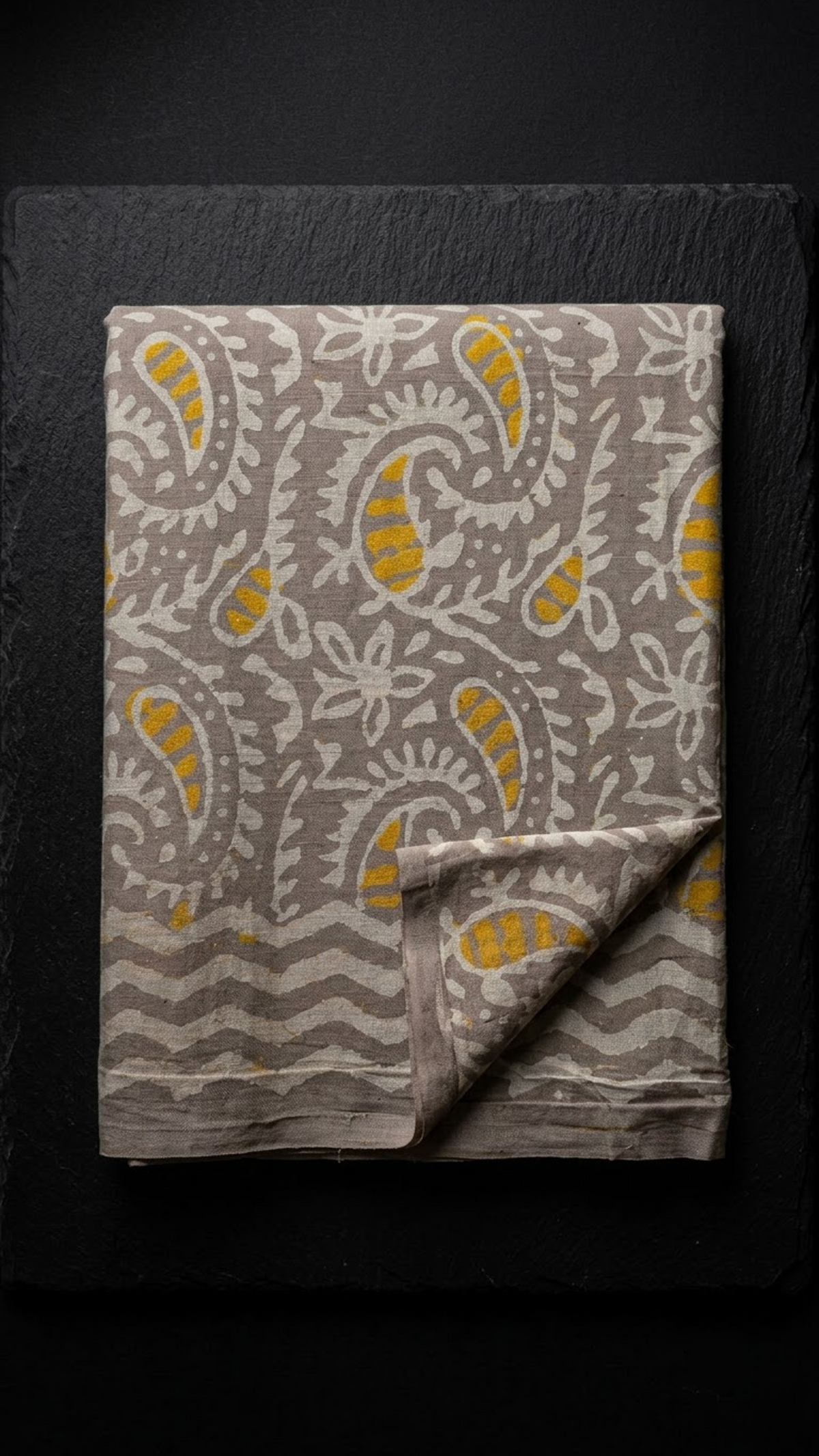 Grey cotton saree with yellow-accented ivory paisleys and wavy border, folded on charcoal