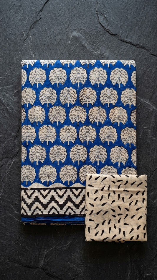 Blue cotton saree with sparse ivory tree motifs and chevron border, folded on charcoal