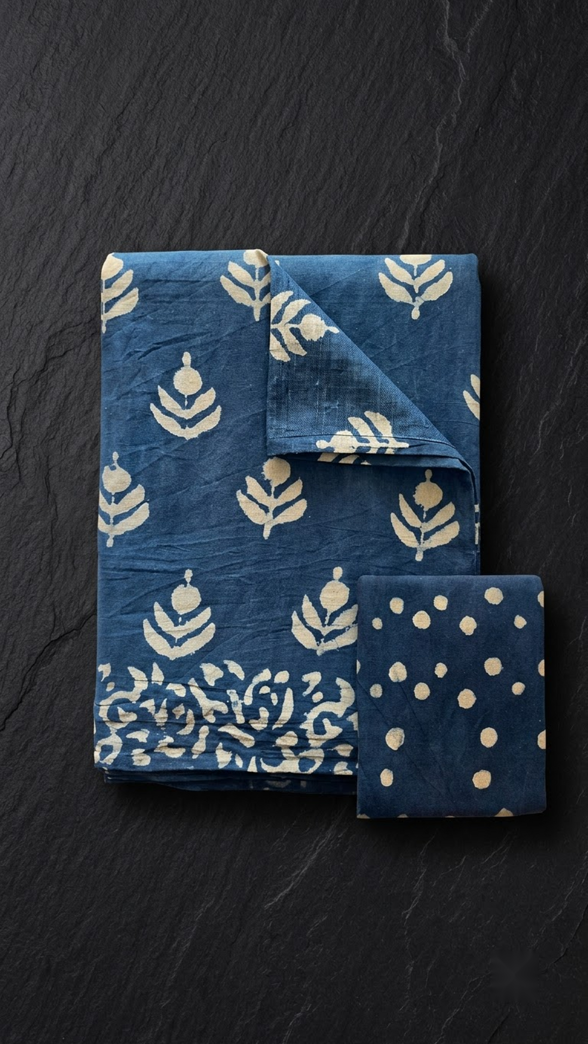 Blue cotton saree with ivory plant sprigs, ivory botanical border, and navy dotted blouse piece, folded on a charcoal background