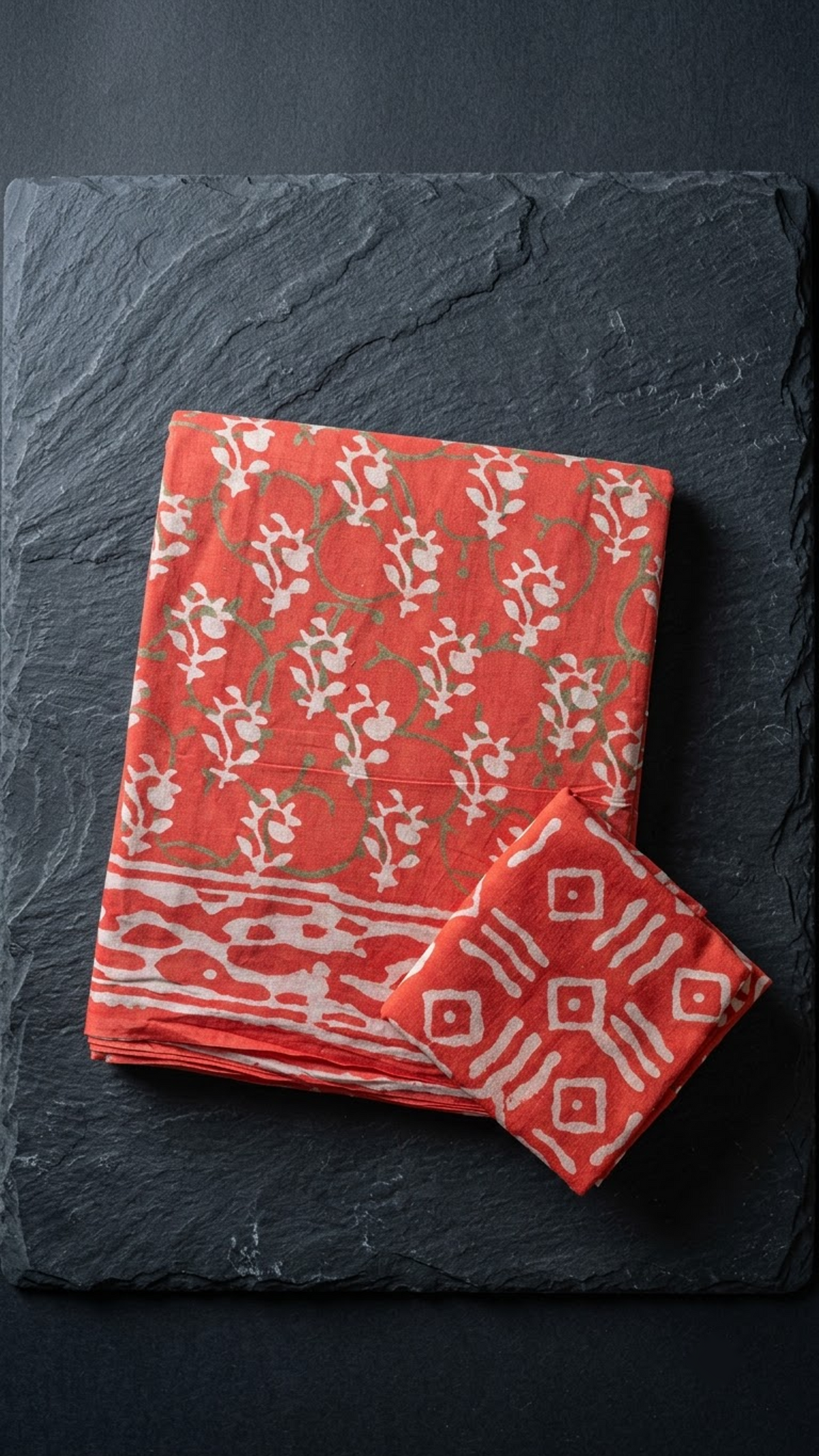 Coral red botanical cotton saree with ivory sprigs and abstract border, folded on charcoal