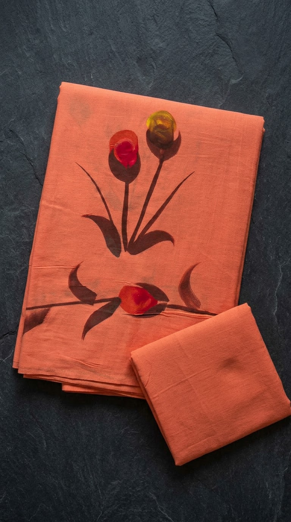 Coral orange cotton saree with flower buds and dark stems, folded on charcoal