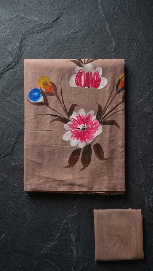 Dusty rose cotton saree with large pink-and-ivory flowers, dark brown leaves, coloured buds, and a plain matching blouse piece, folded on charcoal