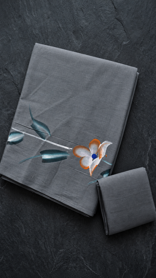 Grey cotton saree with an ivory-and-orange flower, blue centre, deep teal leaves, and a plain matching grey blouse piece, folded on a charcoal background