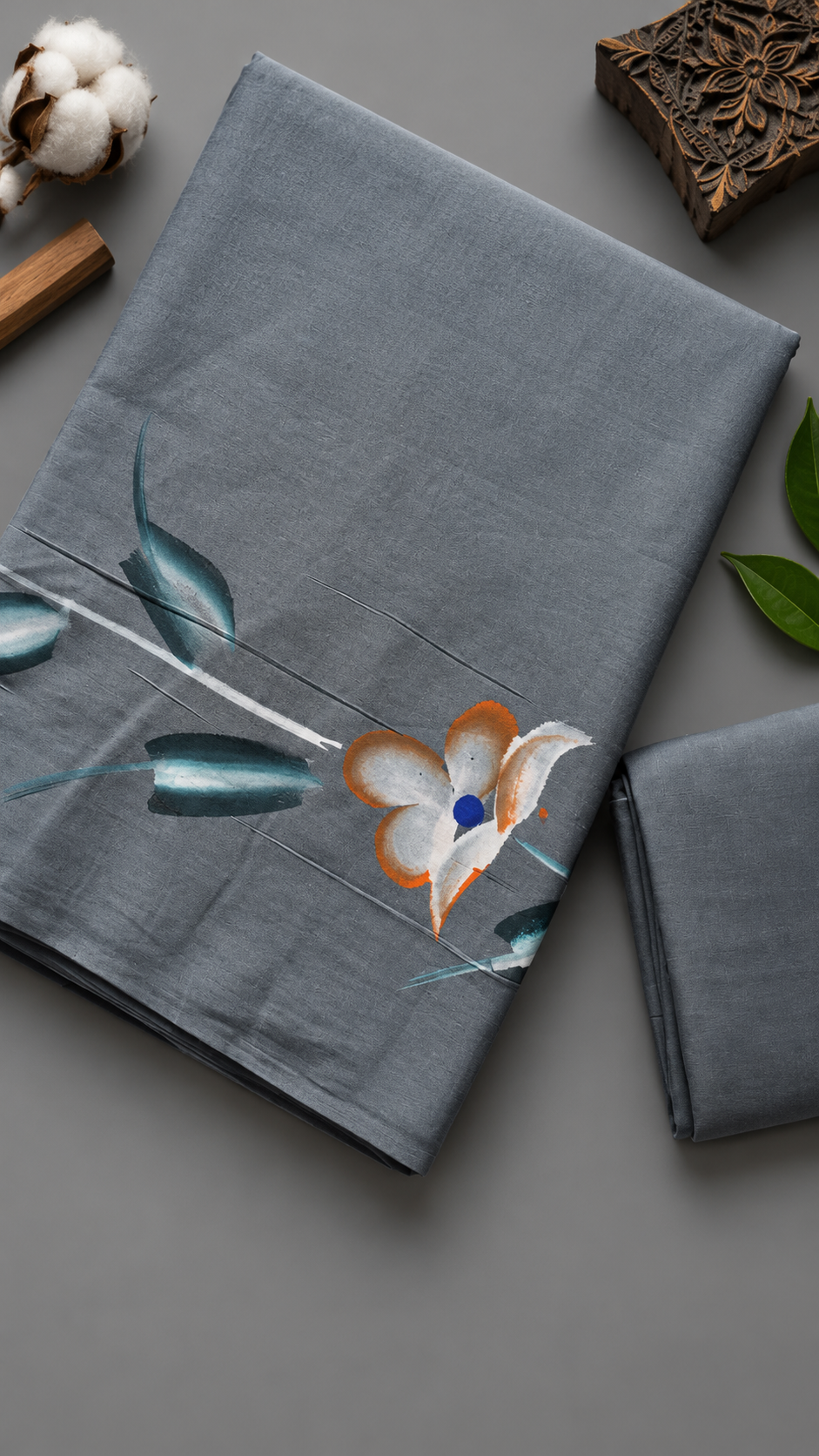 Close detail of the ivory-and-orange flower, blue centre, teal leaves, and slender stems on grey cotton fabric with the plain matching blouse piece