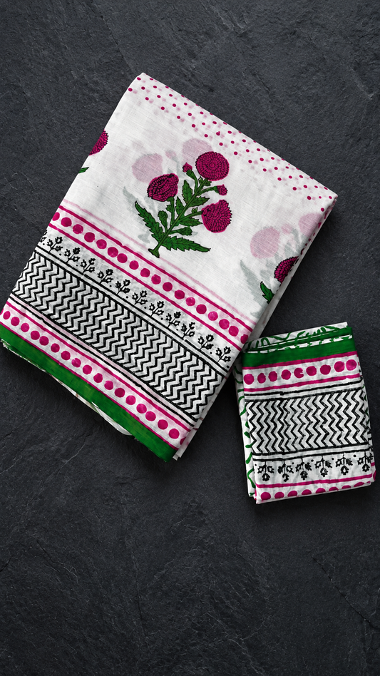Ivory cotton saree with pink polka dots, a pink floral pallu, black zigzag border and green edging, folded on charcoal