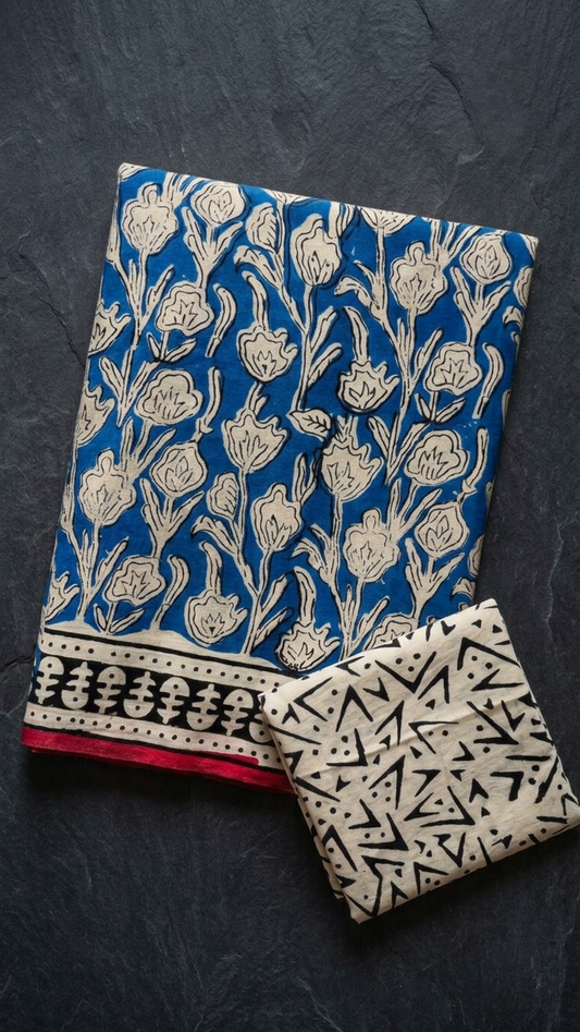 Blue cotton saree with ivory floral vines, a black-and-ivory border with red edging, and an ivory abstract-print blouse piece, folded on a charcoal background