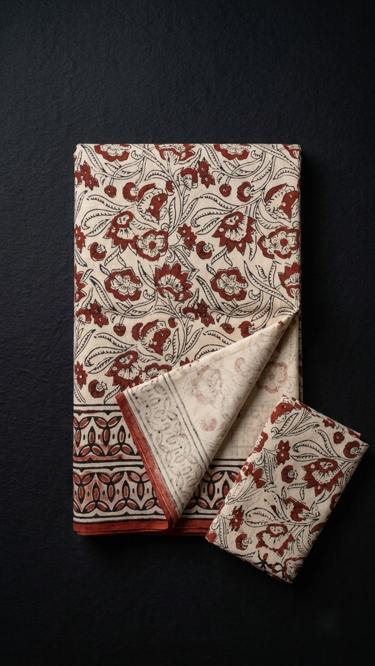 Folded ivory and red floral print cotton saree with blouse piece on a charcoal background