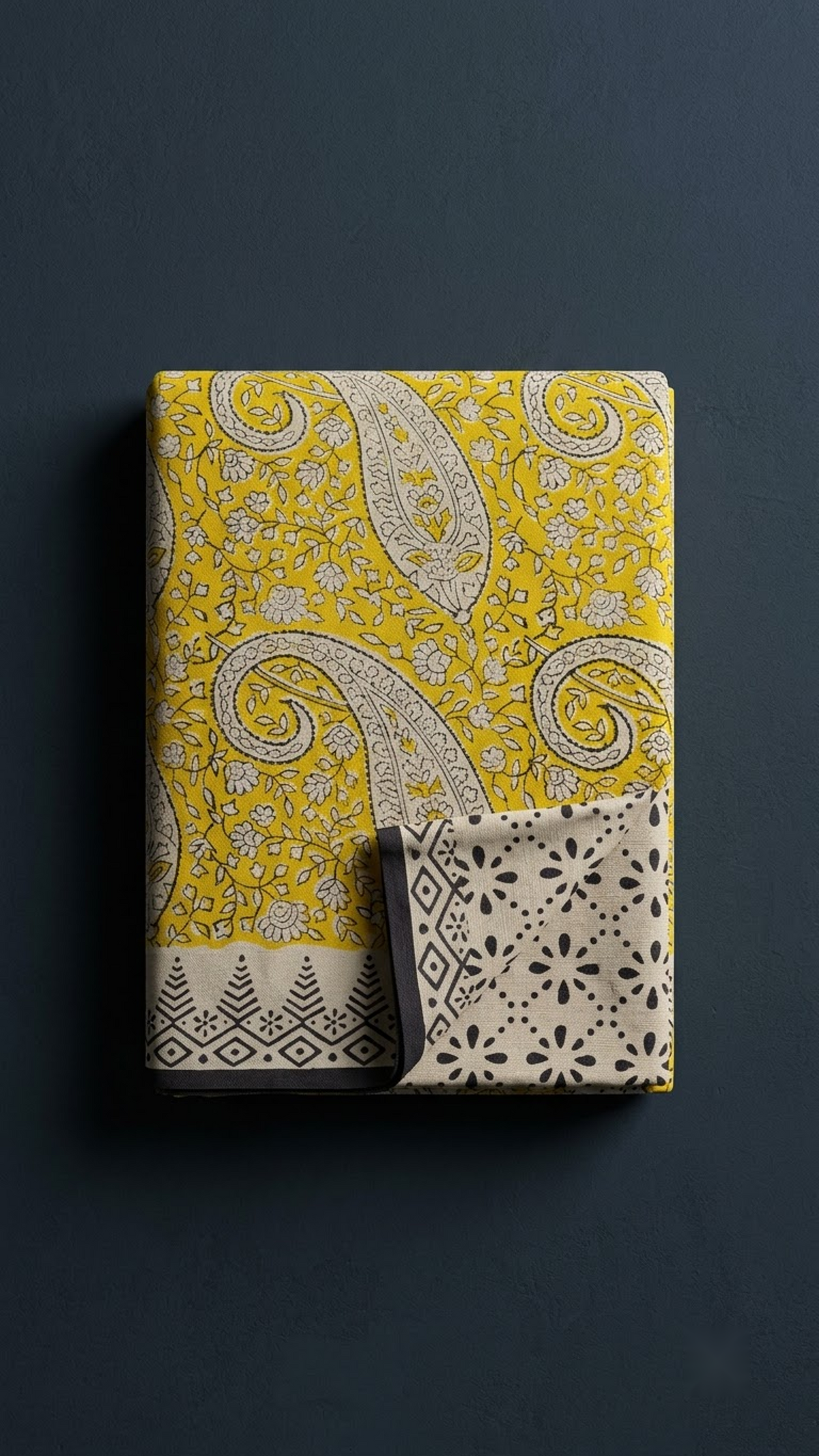 Folded yellow paisley print cotton saree with blouse piece on a charcoal background