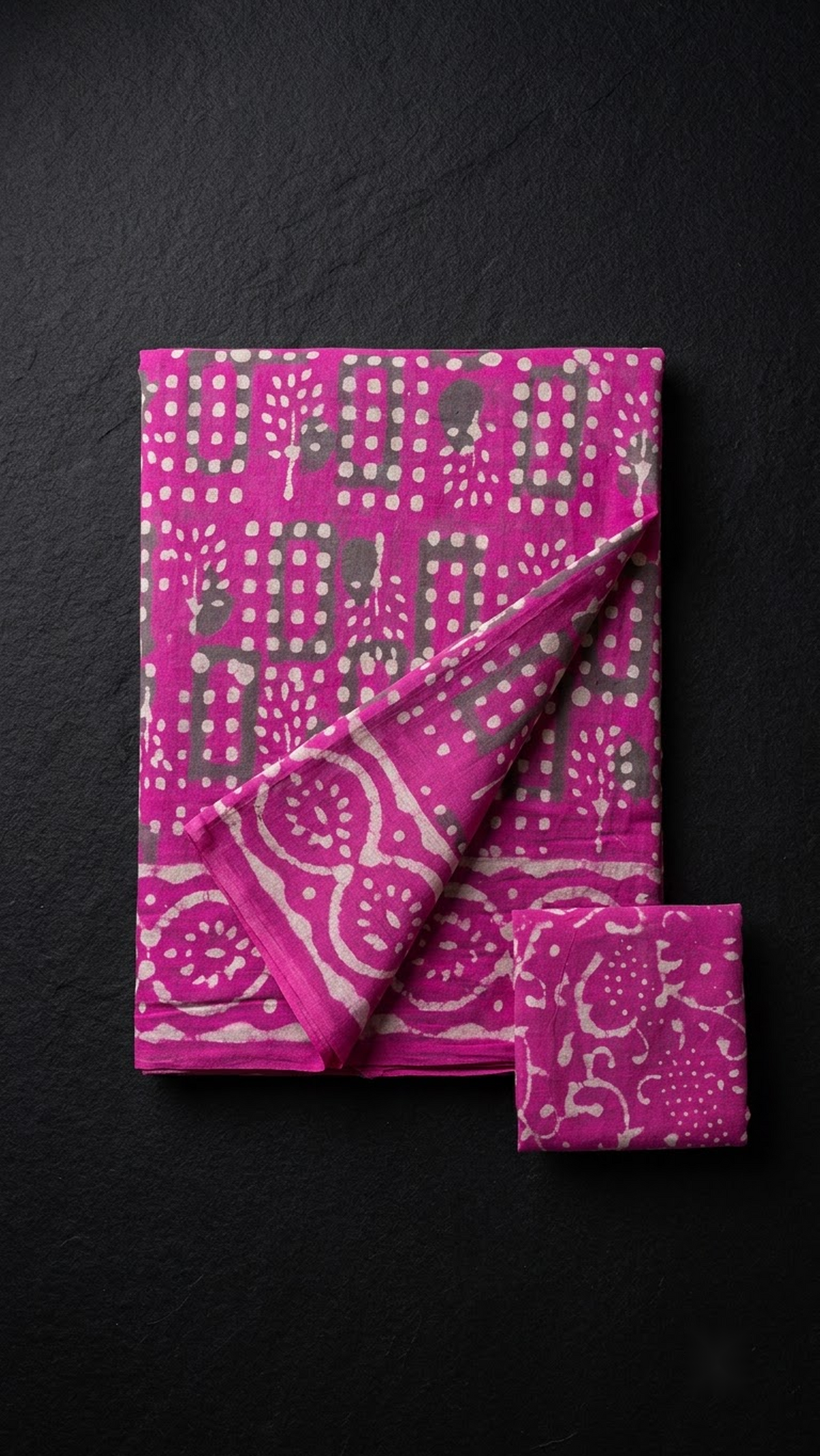Folded magenta geometric print cotton saree with blouse piece on a charcoal background
