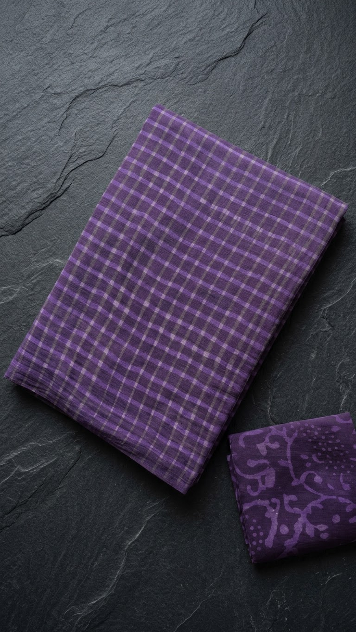 Folded purple check cotton saree with blouse piece on a charcoal background