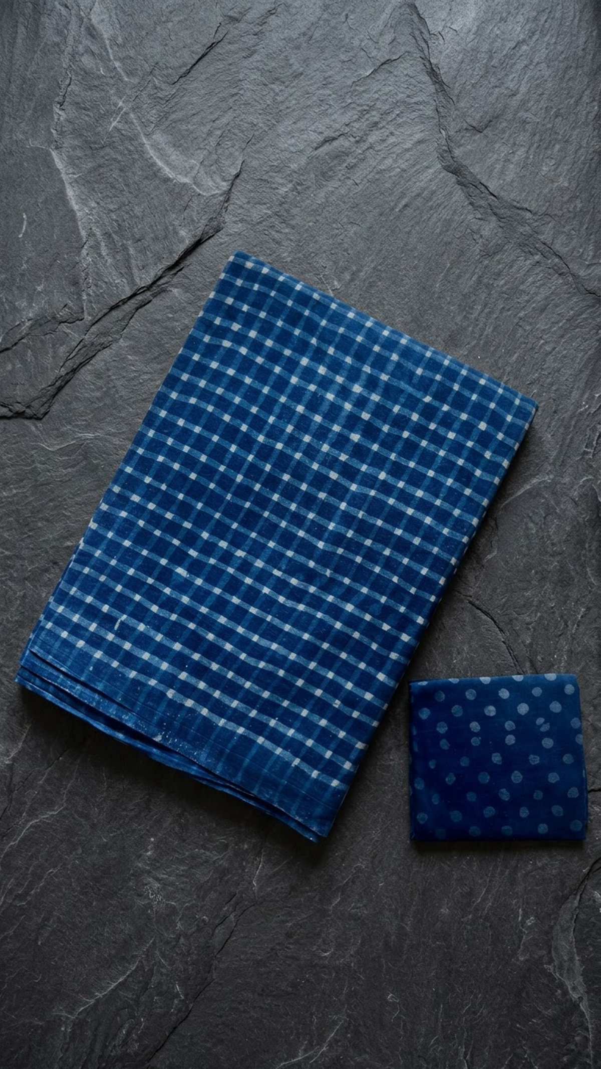 Folded blue check cotton saree with blouse piece on a charcoal background
