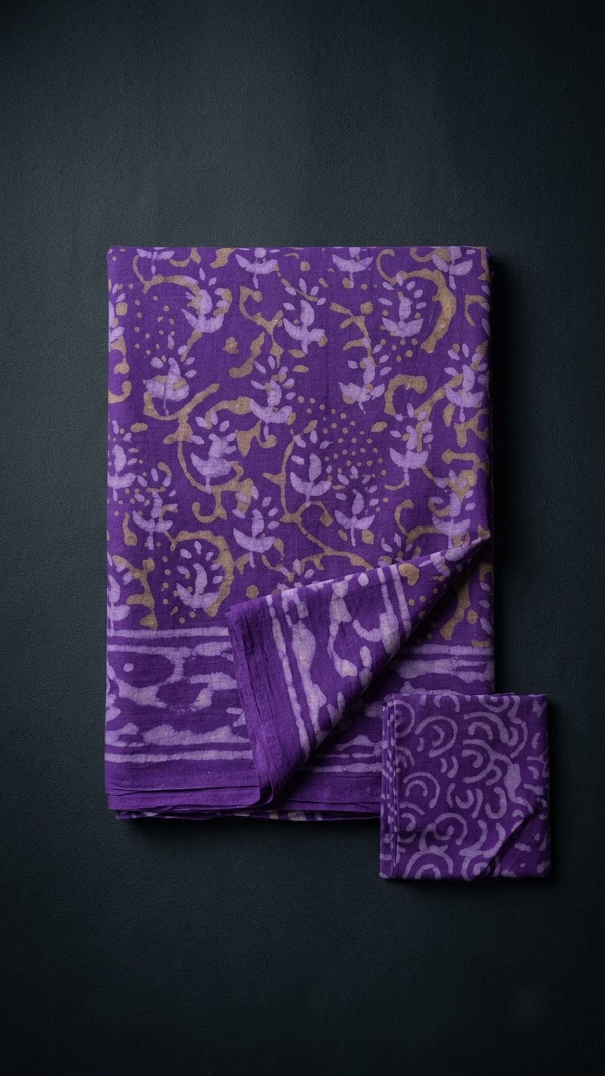 Folded purple floral vine cotton saree with blouse piece on a charcoal background