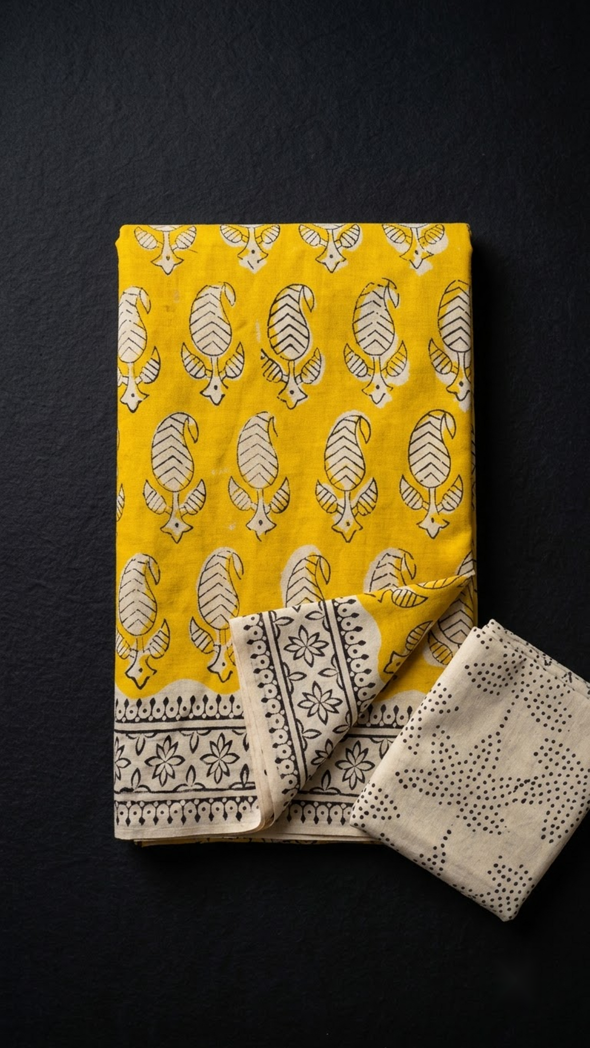 Folded yellow leaf paisley cotton saree with blouse piece on a charcoal background