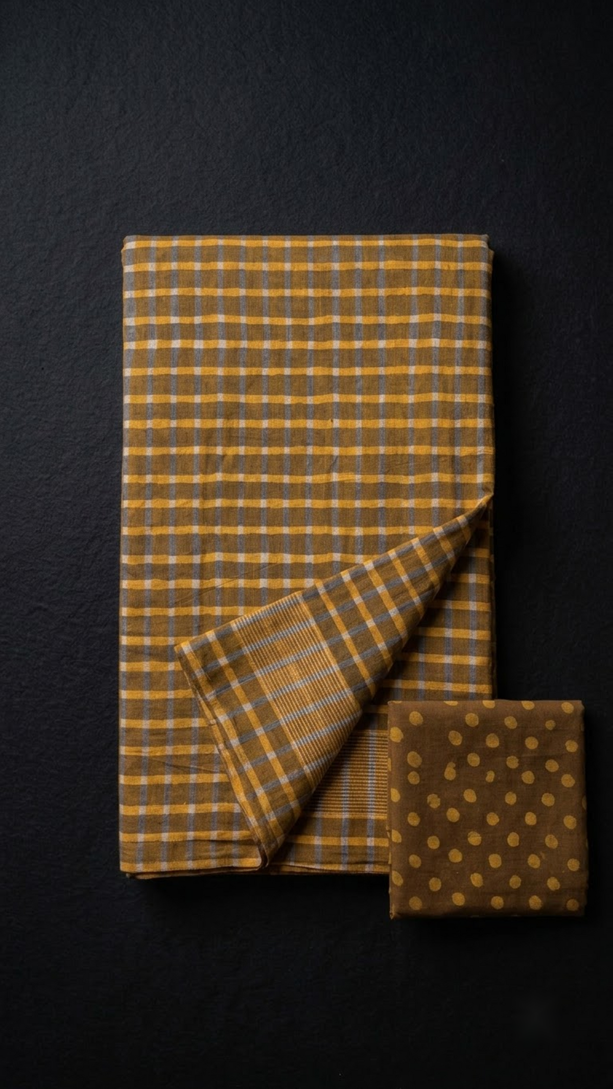 Folded brown and mustard check cotton saree with blouse piece on a charcoal background