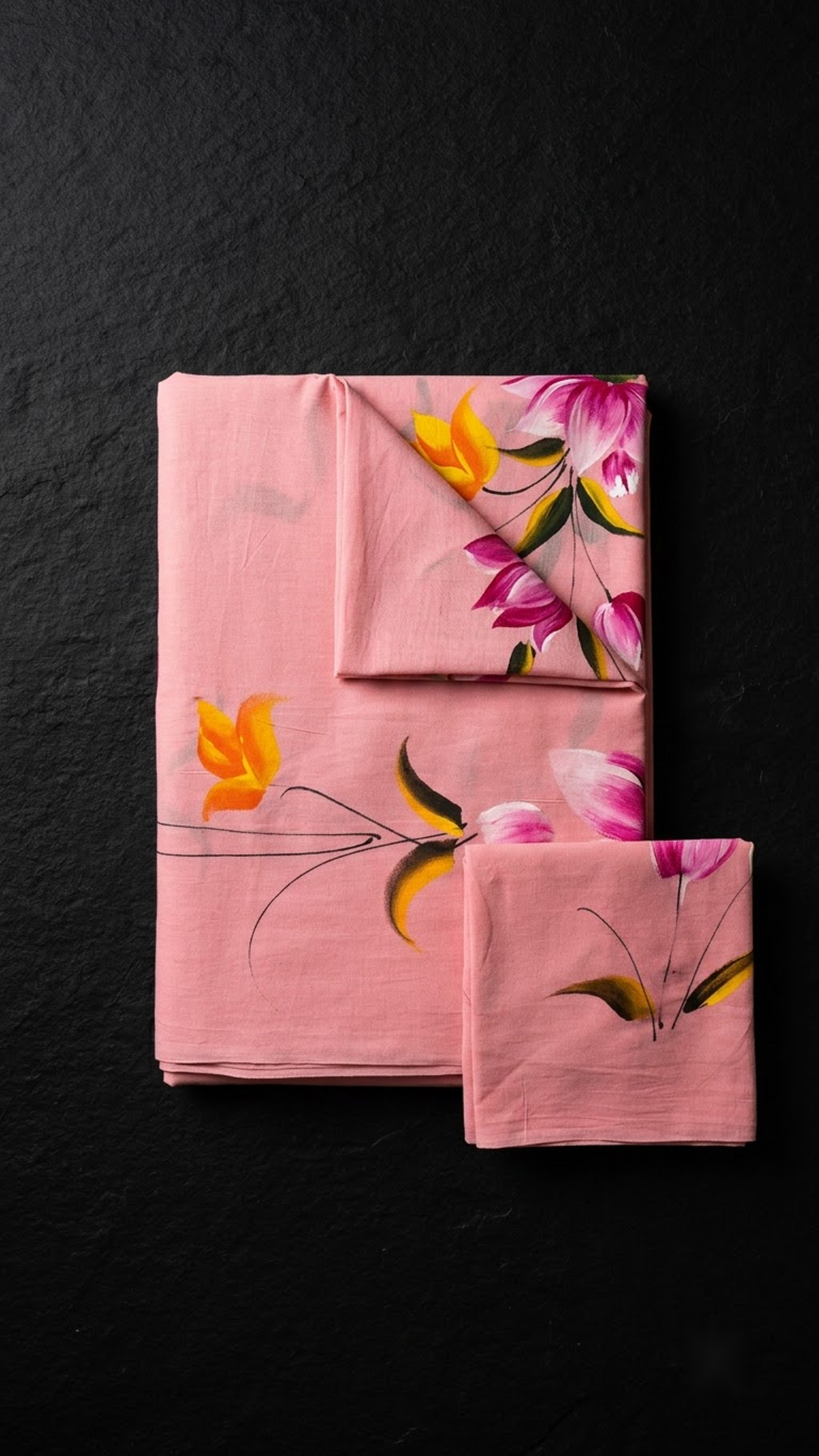 Folded pink floral print cotton saree with blouse piece on a charcoal background