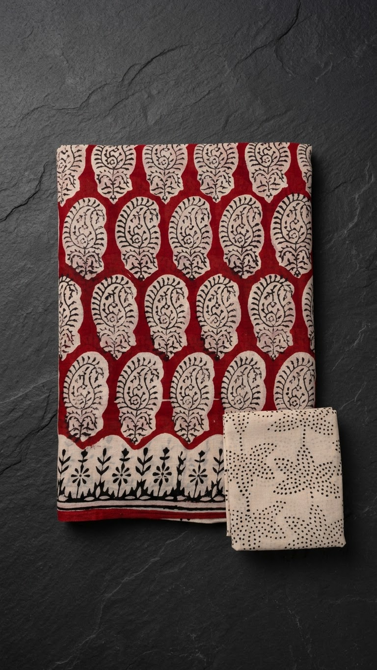Folded red paisley print cotton saree with blouse piece on a charcoal background