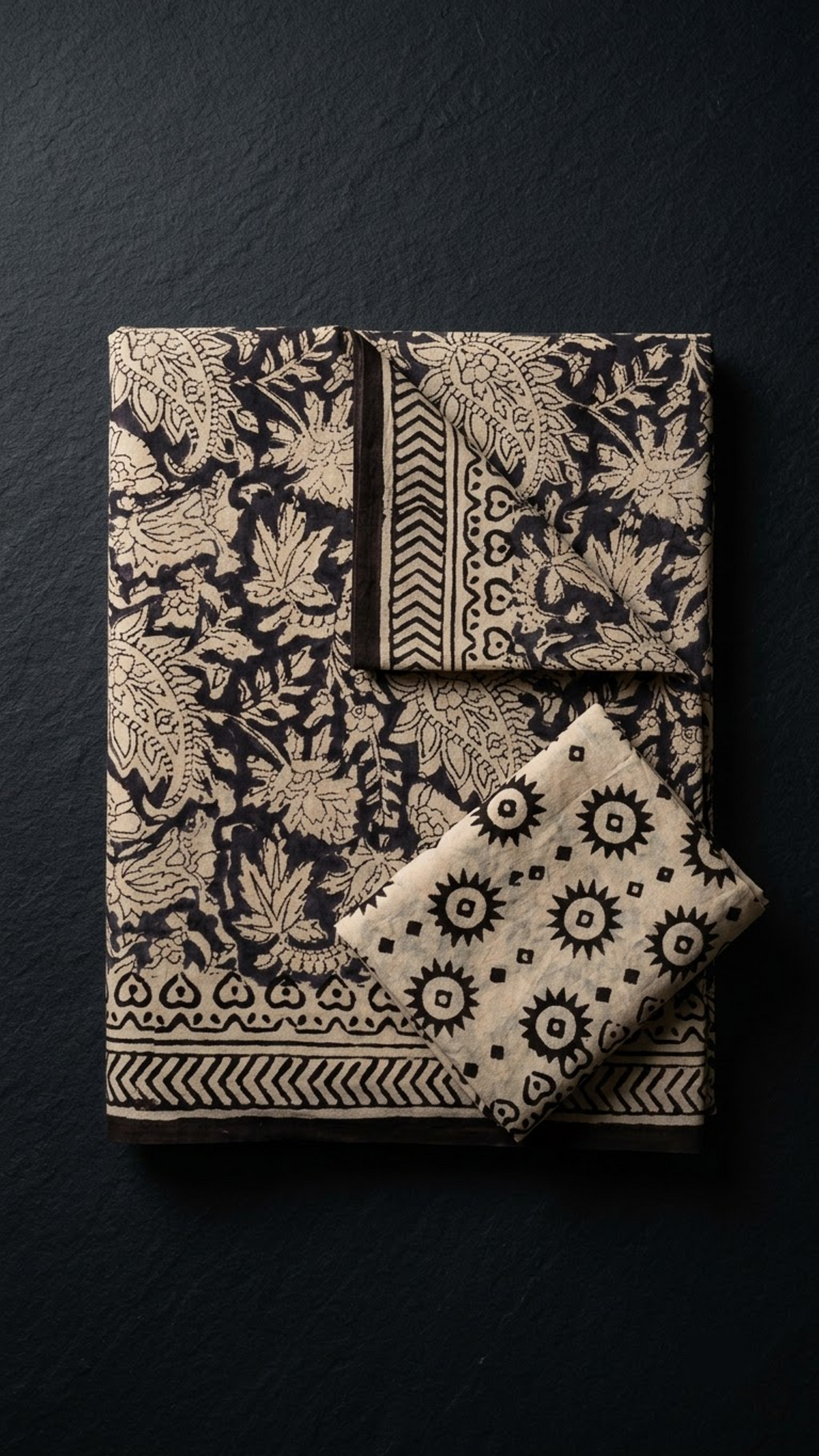Folded dark floral and paisley cotton saree with blouse piece on a charcoal background