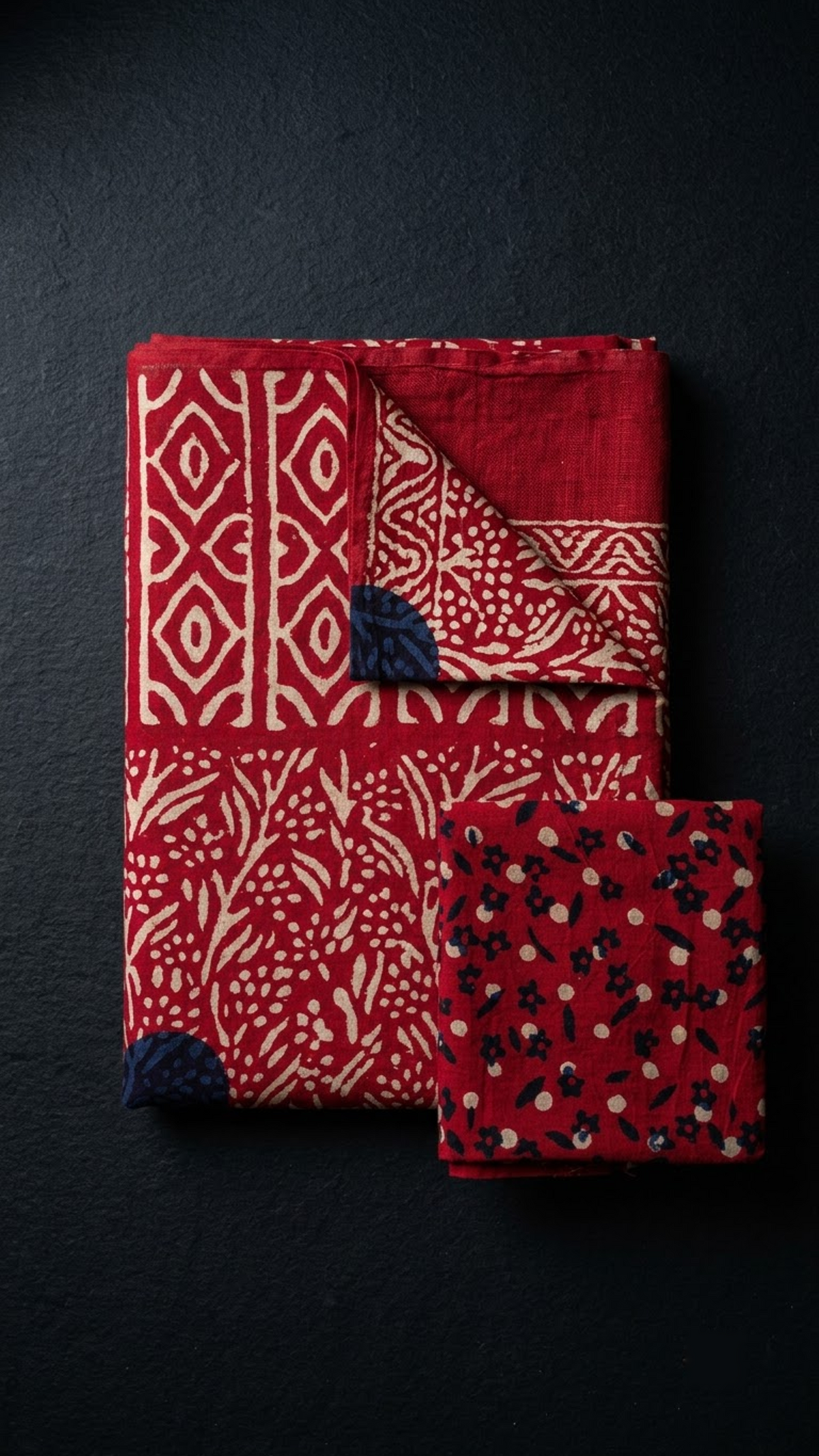 Folded red geometric and botanical cotton saree with blouse piece on a charcoal background