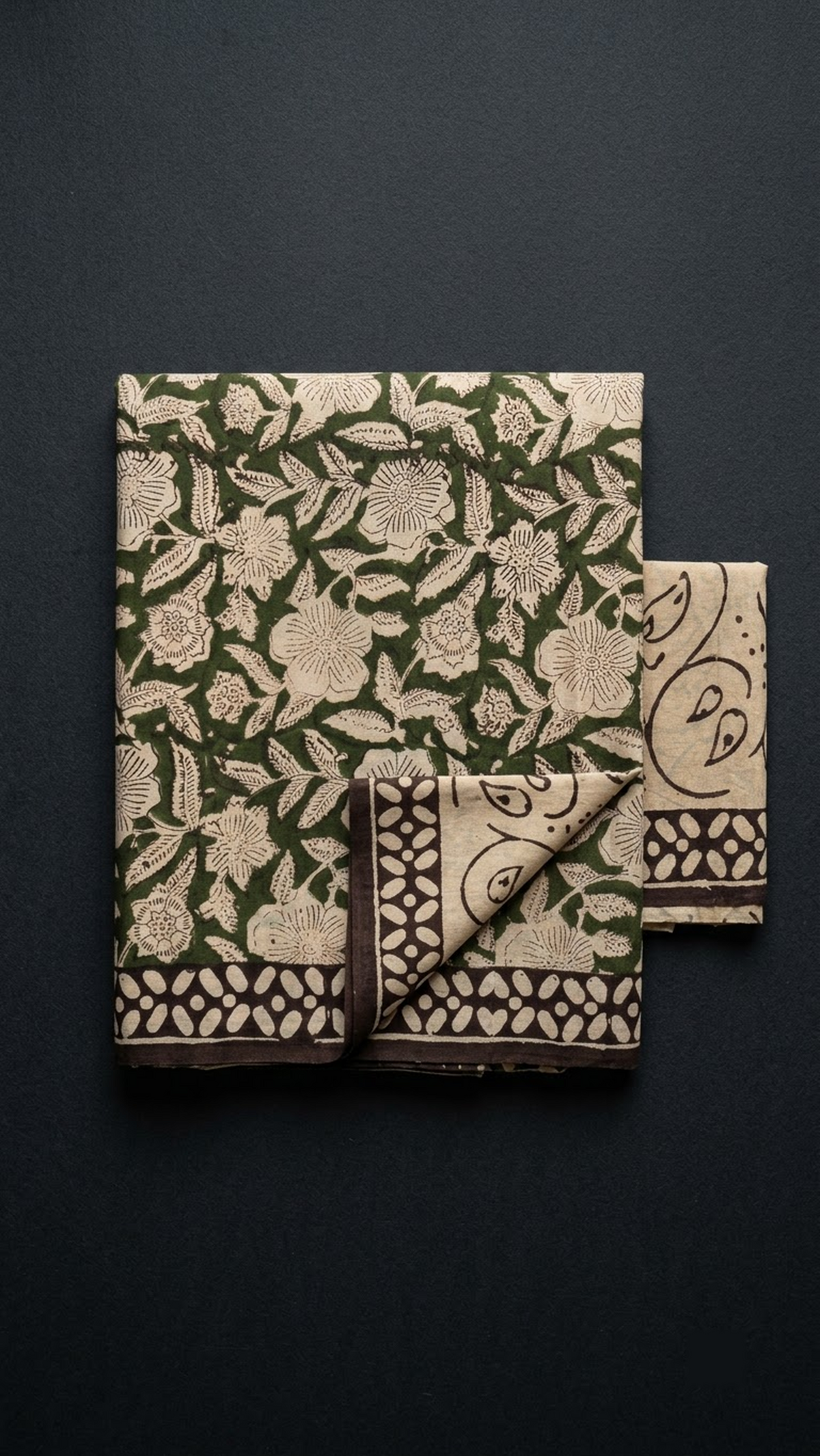 Folded green floral cotton saree with blouse piece on a charcoal background