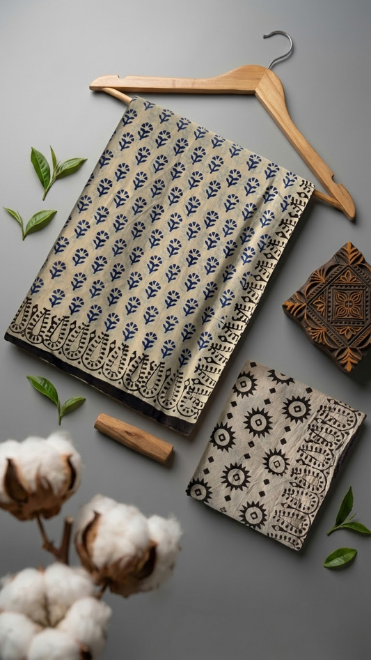 Ivory cotton saree with navy botanical sprigs, a black botanical loop border, and an ivory blouse piece with black starburst and diamond motifs, arranged with the blouse piece in a styled flat lay
