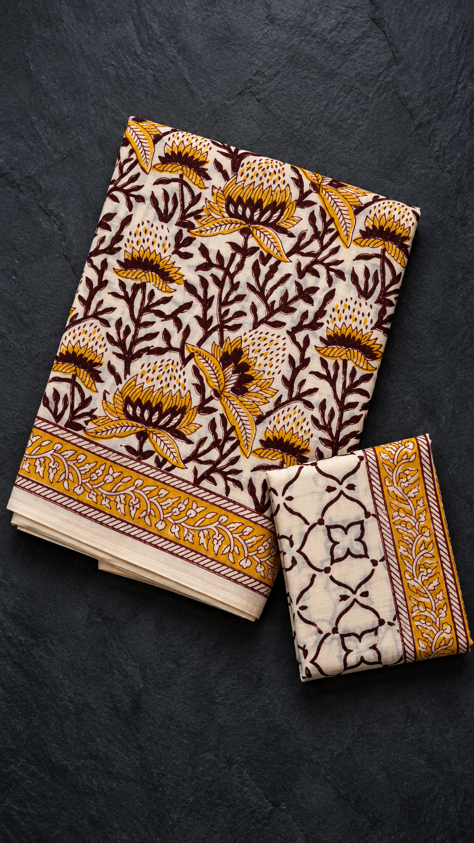 Ivory cotton saree with mustard flowers, maroon leafy branches, a mustard vine border, and an ivory maroon lattice blouse piece, folded on a charcoal background