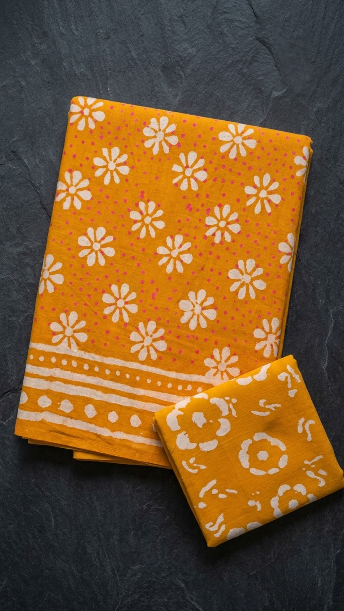 Orange cotton saree with ivory daisy motifs, an ivory striped and dotted border, and an orange circular floral blouse piece, folded on a charcoal background