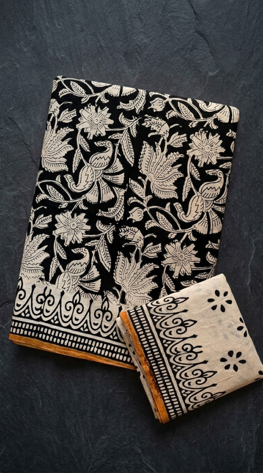 Black cotton saree with ivory bird and floral motifs, an ornamental border with an ochre edge, and an ivory blouse piece, folded on a charcoal background